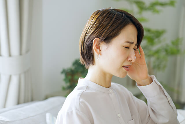 頭痛で頭を押さえる女性