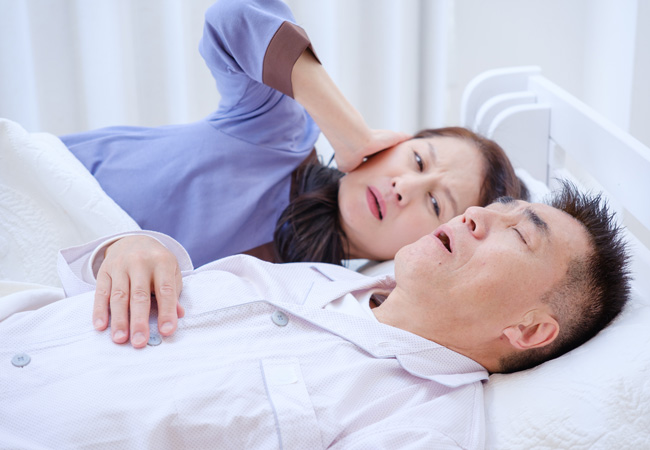 いびきをかいて寝ている男性と耳を抑える女性